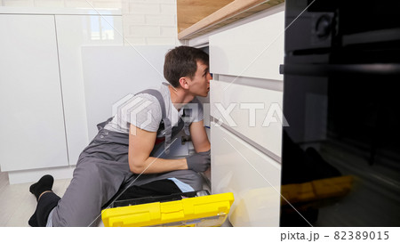 Plumber in grey jumpsuit takes wrench to unscrew detail Plumber in grey jumpsuit takes wrench to unscrew detail 82389015