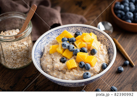 Cooked oatmeal porridge with blueberries and mango Cooked oatmeal porridge with blueberries and mango 82390992