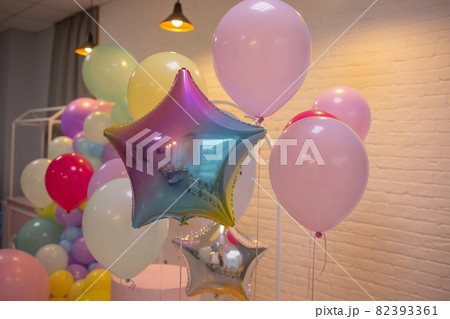 balloons are attached to the railing of the porch. Opening of the store. Cream wall, red staircase. Bright sunlight and shadows. Festive street background. 82393361