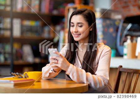 Young happy arab woman using mobile phone, sitting in city cafe and surfing social networks, drinking coffee and resting Young happy arab woman using mobile phone, sitting in city cafe and surfing social networks, drinking coffee and resting 82398469