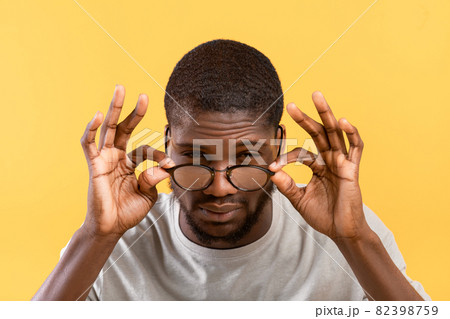 Poor eyesight. African american guy squinting eyes and looking at camera, touching eyeglasses over yellow background Poor eyesight. African american guy squinting eyes and looking at camera, touching eyeglasses over yellow background 82398759