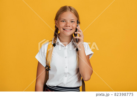 Cheerful smart european young girl student with pigtails and backpack talking on phone Cheerful smart european young girl student with pigtails and backpack talking on phone 82398775