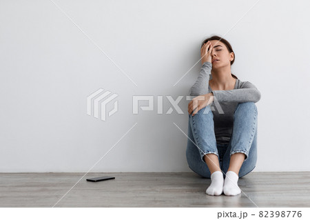 Unhappy caucasian female touching face, sits on floor at home, thinks about problems, upset lady feeling lonely Unhappy caucasian female touching face, sits on floor at home, thinks about problems, upset lady feeling lonely 82398776