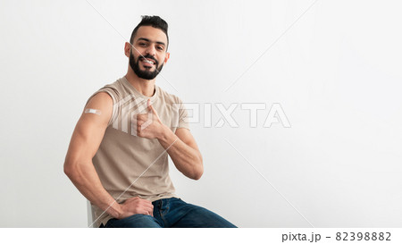 Arab man with adhesive band aid on shoulder after coronavirus vaccination showing thumb up gesture 82398882