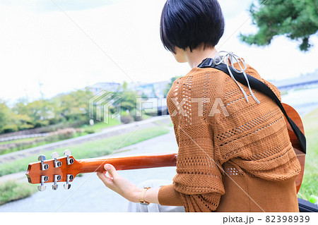 川沿いでアコースティックギターを弾くショートヘアの女性 82398939