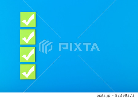 Four white checkmarks on green tablets in a row against blue background with copy space 82399273