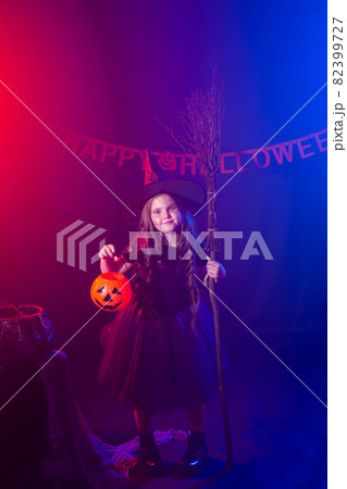 Little girl holds broom on Halloween holiday. Kid girl wear witch costume. Fantasy, fairy tale and masquerade concept. 82399727