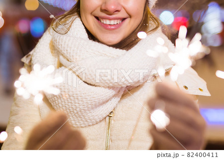 Young beautiful woman in knitted hat and scarf standing in the city with bengal light, sparkler. Concept celebration and christmas. 82400411