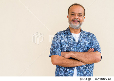 Portrait of happy bearded Indian man smiling against plain wall Portrait of happy bearded Indian man smiling against plain wall 82400538