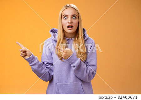 Wow astonished impressed good-looking blond european female in hoodie pop eyes wondered surprised questioned drop jaw pointing left excited asking if gossip true, standing orange background 82400671