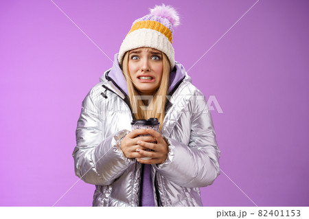 Shaking uncomfortable displeased girl wearing stylish silver jacket hat trembling freezing cold warm hands holding take-away coffee cup clench teeth pop eyes discomfort, standing purple background Shaking uncomfortable displeased girl wearing stylish silver jacket hat trembling freezing cold warm hands holding take-away coffee cup clench teeth pop eyes discomfort, standing purple background 82401153