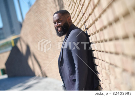 An african american man in a suit standing near the brick wall An african american man in a suit standing near the brick wall 82405995