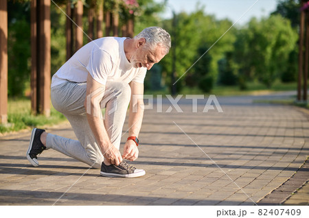 A mid aged man in sportswear lacing his snickers A mid aged man in sportswear lacing his snickers 82407409