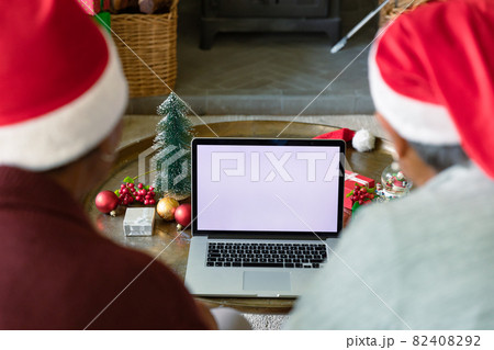 Two diverse senior female friends wearing santa hats using laptop with copy space at christmas time 82408292