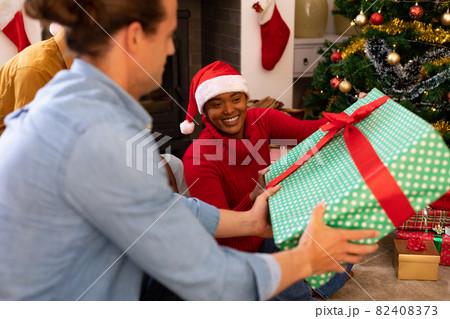 Happy diverse female and male friends sharing presents at christmas time Happy diverse female and male friends sharing presents at christmas time 82408373