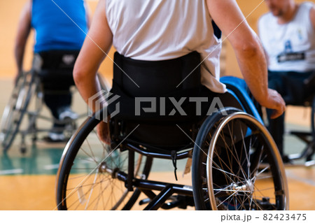Close up photo of wheelchairs and handicapped war veterans playing basketball on the court 82423475