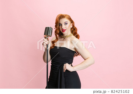 Cropped studio portrait of expressive beautiful female singer on stage giving performance isolated over pink background. Burlesque 82425102