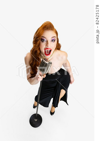Top view full-length portrait of beautiful red-haired woman singing in microphone isolated over white background Top view full-length portrait of beautiful red-haired woman singing in microphone isolated over white background 82425178