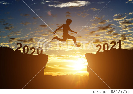 Silhouette of young man jump between 2020 and 2021 years, over the sunset and through gap of hill Silhouette of young man jump between 2020 and 2021 years, over the sunset and through gap of hill 82425759