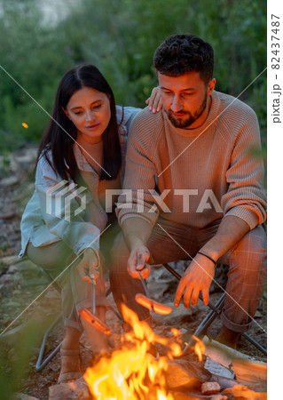 Young affectionate couple frying sausages over fire 82437487