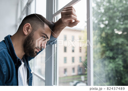 Sad unhappy young handsome man with hand on glass in kitchen interior 82437489