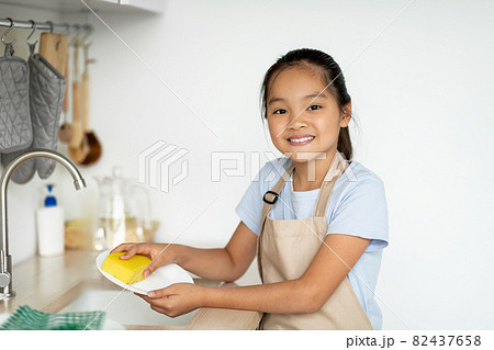 Little housekeeper. Happy asian girl helping mother in kitchen, washing and wiping dishes, standing in kitchen Little housekeeper. Happy asian girl helping mother in kitchen, washing and wiping dishes, standing in kitchen 82437658