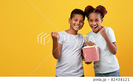 Emotional afro-american siblings watching cartoon together, eating popcorn 82438121