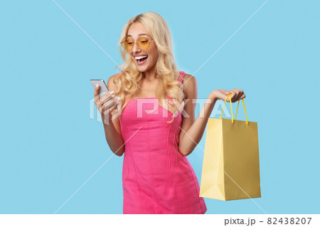 Happy woman using smartphone, holding shopping bags 82438207