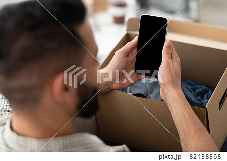 Unrecognizable young Arab guy holding smartphone with mockup for app or website on screen while unboxing parcel at home Unrecognizable young Arab guy holding smartphone with mockup for app or website on screen while unboxing parcel at home 82438368