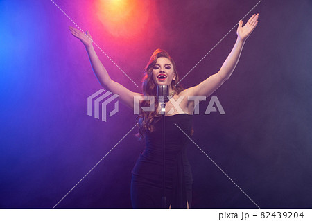 Cropped image of beautiful talented stage singer isolated over gradient blue purple background in neon light with stage smoke Cropped image of beautiful talented stage singer isolated over gradient blue purple background in neon light with stage smoke 82439204