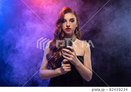 Side view portrait of beautiful femalesinging isolated over gradient blue purple background in neon light with stage smoke Side view portrait of beautiful femalesinging isolated over gradient blue purple background in neon light with stage smoke 82439234