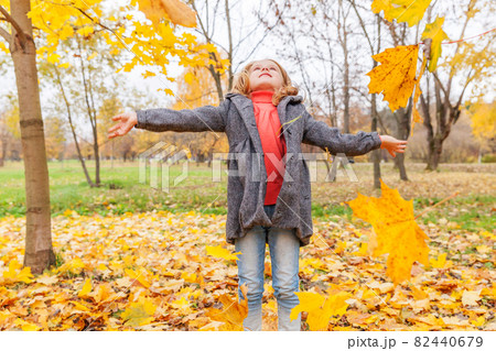 Happy young girl playing under falling yellow leaves in beautiful autumn park on nature walks outdoors. Little child throws up autumn orange maple leaves. Happy young girl playing under falling yellow leaves in beautiful autumn park on nature walks outdoors. Little child throws up autumn orange maple leaves. 82440679