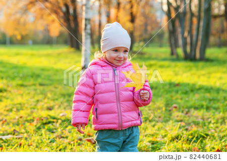 Happy young girl smiling in beautiful autumn park on nature walks outdoors. Little child playing with falling yellow maple leaf in autumn fall orange yellow background. Hello autumn concept. Happy young girl smiling in beautiful autumn park on nature walks outdoors. Little child playing with falling yellow maple leaf in autumn fall orange yellow background. Hello autumn concept. 82440681