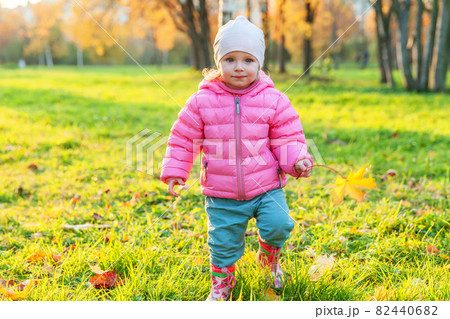 Happy young girl smiling in beautiful autumn park on nature walks outdoors. Little child playing with falling yellow maple leaf in autumn fall orange yellow background. Hello autumn concept. 82440682