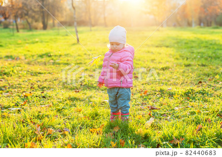 Happy young girl smiling in beautiful autumn park on nature walks outdoors. Little child playing with falling yellow maple leaf in autumn fall orange yellow background. Hello autumn concept. Happy young girl smiling in beautiful autumn park on nature walks outdoors. Little child playing with falling yellow maple leaf in autumn fall orange yellow background. Hello autumn concept. 82440683