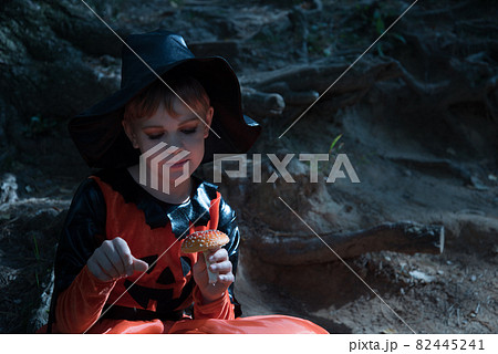 Portrait of a witch. A girl dressed as a witch holds an amanita in her hand. A mushroom for a witch's potion. Beautiful stylish picture in the forest Portrait of a witch. A girl dressed as a witch holds an amanita in her hand. A mushroom for a witch's potion. Beautiful stylish picture in the forest 82445241