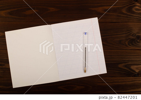 School notebook with oblique lines, transparent pen on the table brown wooden background. Blank sheet of paper in notebook on the desk. Back to school. School supplies. Top view. Copy space for text School notebook with oblique lines, transparent pen on the table brown wooden background. Blank sheet of paper in notebook on the desk. Back to school. School supplies. Top view. Copy space for text 82447201