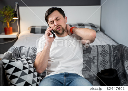 Disabled painful man with neck brace talking on phone at home. Man with spine trauma in neck brace cervical call insurance company for medical help. Male with neck injury calls doctor after accident Disabled painful man with neck brace talking on phone at home. Man with spine trauma in neck brace cervical call insurance company for medical help. Male with neck injury calls doctor after accident 82447601