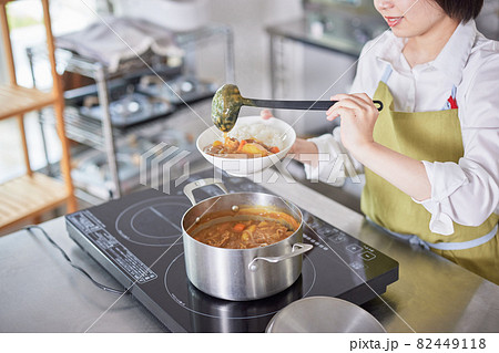 キッチンでカレーをご飯に盛るエプロン姿の若い女性 82449118