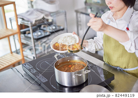 キッチンでカレーをご飯に盛るエプロン姿の若い女性 82449119