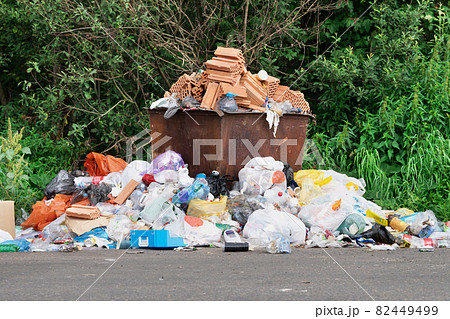 Rusty trash can overflowed with rubbish on the roadside 82449499
