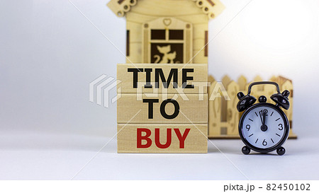 Time to buy real estate. Wooden blocks form the words 'time to buy' near miniature house. Black alarm clock. Beautiful white background. Business concept. Copy space. 82450102