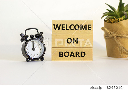 Welcome on board symbol. Wooden blocks with words 'Welcome on board'. Beautiful white background, black alarm clock, house plant. Business, welcome on board concept, copy space. Welcome on board symbol. Wooden blocks with words 'Welcome on board'. Beautiful white background, black alarm clock, house plant. Business, welcome on board concept, copy space. 82450104