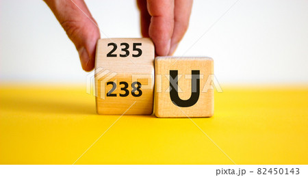 Uranium enrichment symbol. Hand turns the cube and changes the word '238 U' to '235 U'. Beautiful yellow, white background, copy space. Business, nuclear technology and uranium enrichment concept. Uranium enrichment symbol. Hand turns the cube and changes the word '238 U' to '235 U'. Beautiful yellow, white background, copy space. Business, nuclear technology and uranium enrichment concept. 82450143