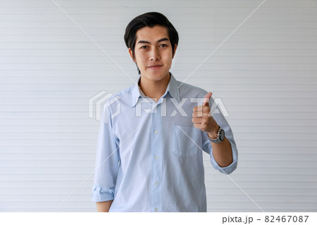 20s handsome professional successful business working man or employee wearing formal shirt, smiling with happiness and satisfaction, making gesture great thumb up, standing indoor office or workplace. 82467087