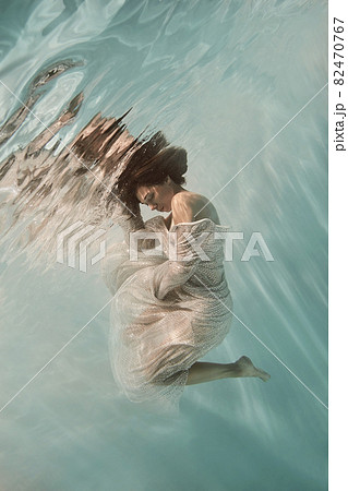 A girl in a blue dress swims underwater on a light background as if in weightlessness A girl in a blue dress swims underwater on a light background as if in weightlessness 82470767