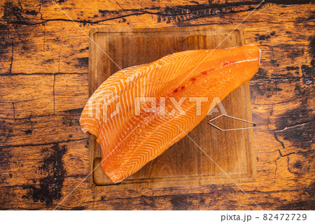Large raw salmon fillet on a wooden board with fish bone pliers Large raw salmon fillet on a wooden board with fish bone pliers 82472729