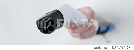 Male hand holds car plug for charging electric vehicles 82475433