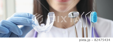 Smiling female doctor holds transparent plastic mouth guard and stomatological instruments in her hand 82475434