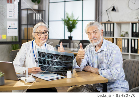 Mature doctor and patient sitting at cabinet with x ray scan Mature doctor and patient sitting at cabinet with x ray scan 82480770